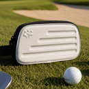 White golf bag with black strap on a golf course with golf balls and club.